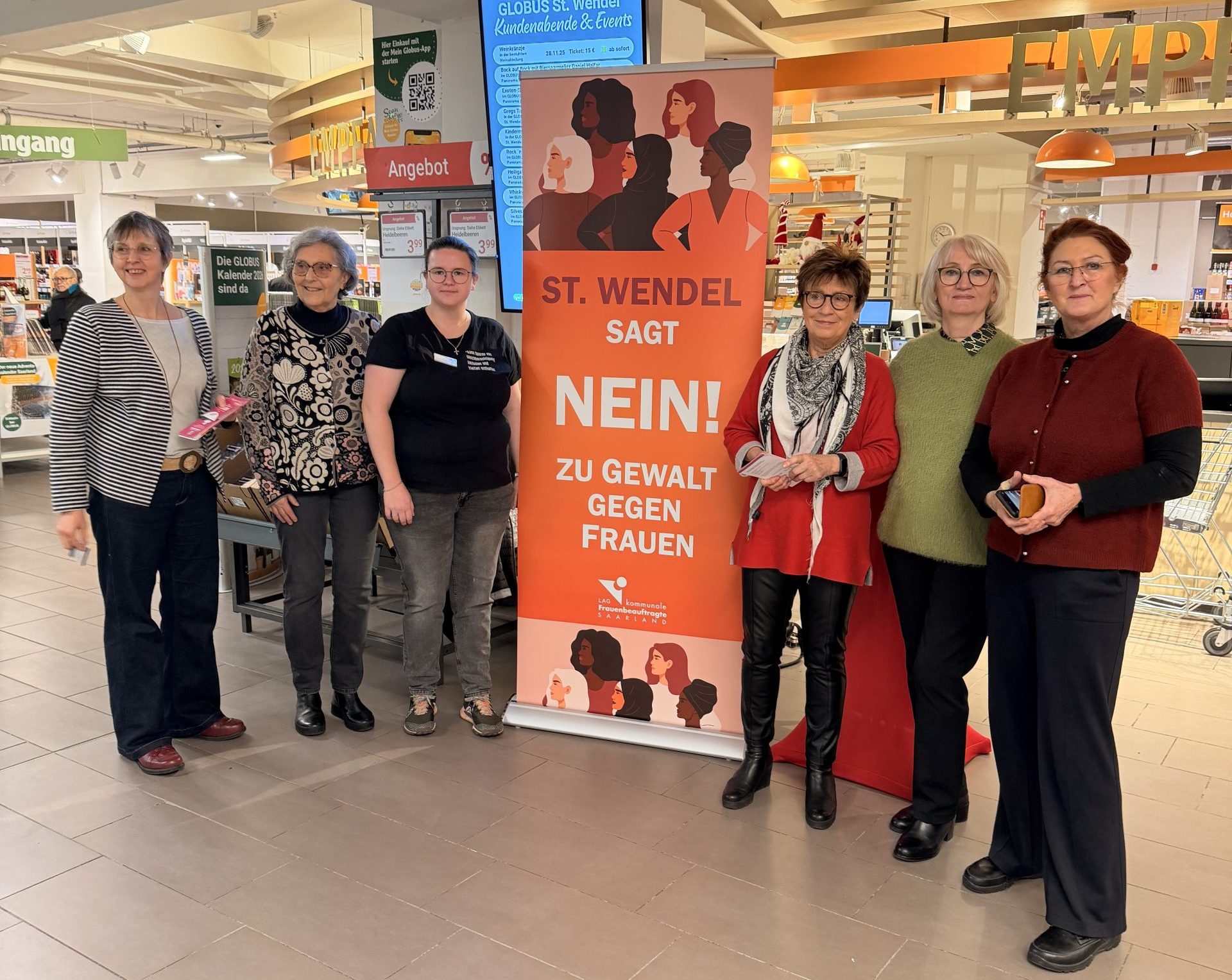 Gruppenfoto Frauenbeauftragte der Kreisstadt St. Wendel mit den Frauen des Landkreises St. Wendel im Globus Markt mit dem Aufsteller des Aktionstages gegen Gewalt an Frauen